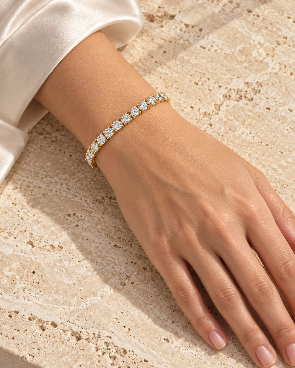 Gold moissanite tennis bracelet on a wrist resting on travertine