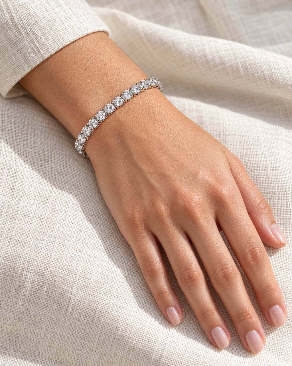 Silver moissanite tennis bracelet on a wrist resting on linen